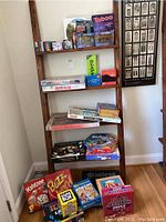 Full view of ladder shelf with multiple boxed board games, puzzles, and card games including Yahtzee, Monopoly, Taboo, and Buzz Word.