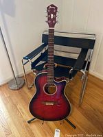 Full view of the Ibanez acoustic-electric guitar, showing reddish sunburst finish, cutaway body, fretboard, and black metal stand.