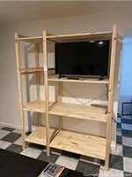 Full view of assembled IKEA Hejne pine wood bookcase with two sections: narrow on left and wide on right, three shelves each, holding a TV on top shelf.