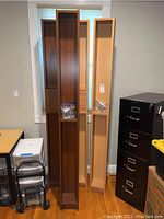 Four IKEA media storage towers in two wood finishes, leaned against wall with bags of shelving pins and additional fixed shelves inside.