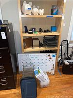 Wide view of shelving unit with office supplies including piggy banks, organizers, laptop bag, and whiteboard