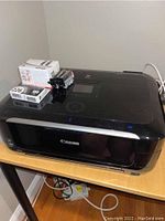 Front view of Canon MG6220 printer with several ink cartridges and boxes on top.