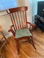 Full view of wooden rocking chair with vertical slat back, armrests, and green cushion on seat.