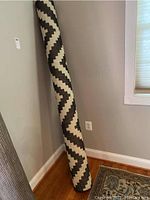 Rolled up IKEA rug with a zigzag black and white pattern, leaning against a wall on hardwood floor.