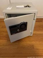 Front angle showing open safe door with combination dial and key lock, keys on top of safe.