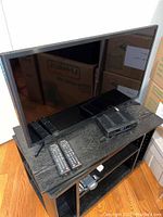 Front view of Samsung 32" TV on black console table with two remote controls and a connected device on top.