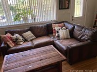 Full view of brown leather sectional with pillows and coffee table