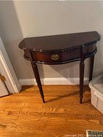 Full frontal view of a dark wood half moon table with tapered fluted legs and a single drawer with brass oval pull.