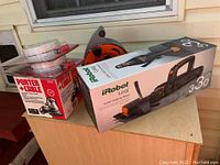Lot contents showing boxed iRobot Looj gutter cleaning robot, Porter Cable orbit sander box, Kiddie smoke alarms in packaging, and black-orange cord reel.