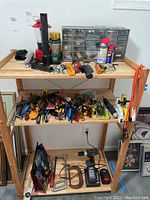 Wide shot showing wooden shelves with assorted hand tools, power drill, battery charger, flashlights, and drawer organizer with small hardware.