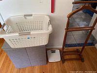 Full view of the double laundry hamper with plastic laundry basket on top, wooden valet stand beside it, and digital scale on the floor.