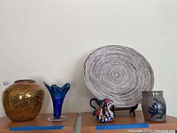 Photo showing five pottery items including four vases/pitcher/crock and one decorative plate on stand arranged on shelves