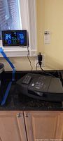 Bose Wave Radio CD player with remote and digital weather station on kitchen counter near window.