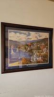 Front view of a framed print showing a coastal village with boats and houses under a cloudy sky
