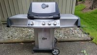 Photo showing full front view of Ultra Chef stainless steel outdoor propane grill with four knobs, dual side shelves, and wheels for mobility.