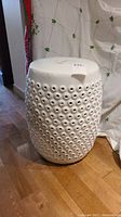 Full side view of the white ceramic garden stool showing the eyelet pattern.