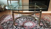 Front view of glass top coffee table on a patterned rug, showing the table's shape and metal frame