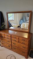 Wooden dresser with nine drawers and matching mirror, showing front view and wooden details.