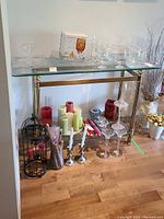 Full view of gold metal-framed glass top table with bevelled edges. Table holds various glassware and candles in the surrounding area.