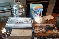 Photo showing all items including the 3-tier stainless steel steamer, boxed Dual Ice Shaver, boxed crepe maker, boxed Pampered Chef mandoline, stainless steel food warmer, and metal food cover.