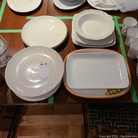 Top view showing multiple white serving plates and dishes, including a rectangular plate with a lemon decoration and several white bowls and round plates.