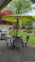 Full view of patio set including table with glass top, green umbrella, and four plastic chairs arranged outdoors.