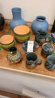 Overview of the pottery set showing vases, pitcher, colorful small decorative vase, mugs, and bowls on blanket