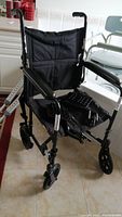Front-angle view of black folding wheelchair with detachable footrests placed on seat showing condition and components.