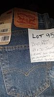 Close-up photo showing Levi Strauss & Co. leather patch on blue denim jeans size 29 with tag attached and handwritten note showing lot details.