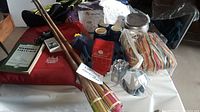 Various camping and hiking items displayed on a table including hiking poles, drink mugs, cloth items, a coffee grinder, and a red bag.