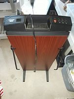 Full view of Corby 7700 pants presser showing wood grain front panel, top control panel, power cord, and metal legs with side hangers.