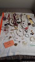 Overview of the costume jewelry laid out on a white sheet showing multiple bead necklaces, bracelets, pendants, pins, earrings, and a watch.