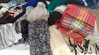 Photo showing assorted used scarves, hats, and belts, including knit and woven scarves in various colors and patterns, knit hats, and leather belts.