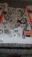 Full view of assorted vintage and costume jewelry spread on white cloth, including necklaces, earrings, rings and bracelets.