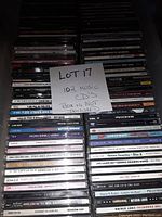 Multiple stacks of 102 music CDs with visible spines and front covers showing various artists and albums. A handwritten note 'LOT 17 102 MUSIC CD'S BOX IS NOT INCLUDED' is placed among the CDs.