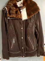 Full front view of the dark brown leather jacket with removable faux fur collar and zipper details.