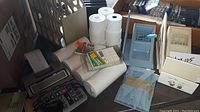 Photo showing large calculator, rolls of white paper, plastic dispensers, box of index cards, and several desk organizers