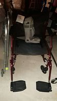 Front view of maroon electric powered wheelchair showing black seat, armrests, footrests, and attached leaflet.