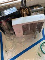 Photo shows stainless steel cocktail tools, boxed Charisma champagne glasses set, metal wine bottle-shaped cork holder, and martini shaker with glasses.