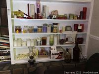Wide view showing shelves holding a variety of candles, wax melts, glass jars, a glass lantern, and boxed firelogs at bottom.