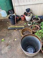 Overview of plastic and ceramic pots leaning against wall outdoors, various sizes and some with plants