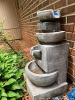 Side view of entire four-tier fountain against brick wall with nearby foliage