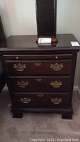 Front view of the dark wood nightstand with brass handles and decorative feet.