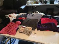 Wide view of folded ladies clothing including shirts, pants, sweaters and camisoles in assorted colors on a white table.