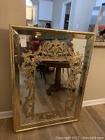 Full front view of the large rectangular decorative mirror with a gold-tone acrylic frame and elaborate ornamental detailing at top and bottom center.