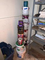Stack of paint and adhesive cans of various sizes and brands in a corner near shelving