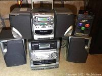 Philips Magnavox AZ 2407 portable CD micro system, Aiwa CA-DW635 stereo component system, Sound Vortex wireless speaker all shown together on a floor.