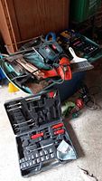 Overview of power tools and various hand tools scattered on and around storage bins including drills and jigsaw