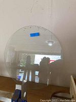 Clear round glass top standing upright against a wall, showing size and shape with some reflections visible.