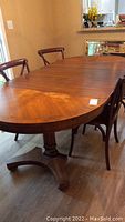 Full view of the solid wood dining table with three leaves installed, showing rounded edges and pedestal leg base.